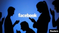 People are silhouetted as they pose with laptops in front of a screen projected with a Facebook logo, file photo. 