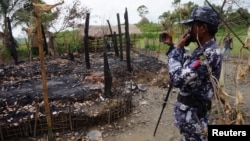 FILE - A Myanmar border guard police officer takes pictures at the remains of a burned house in Tin May village, northern Rakhine state, Myanmar.