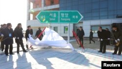 Para pejabat Korea Utara dan Selatan, membuka penutup papan penunjuk arah Seoul ke Pyeongyang dalam acara peletakan batu pertama untuk menghubungkan kembali jalur kereta api dan jalan di Stasiun Panmun di Kaesong, Korea Utara, 26 Desember 2018. (Yonhap via REUTERS)