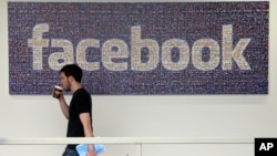 FILE - A Facebook employee walks past a sign at Facebook headquarters in Menlo Park, California. Britain's information commissioner tells BBC on Tuesday she is also investigating Facebook and has asked the company not to pursue its own audit of Cambridge 
