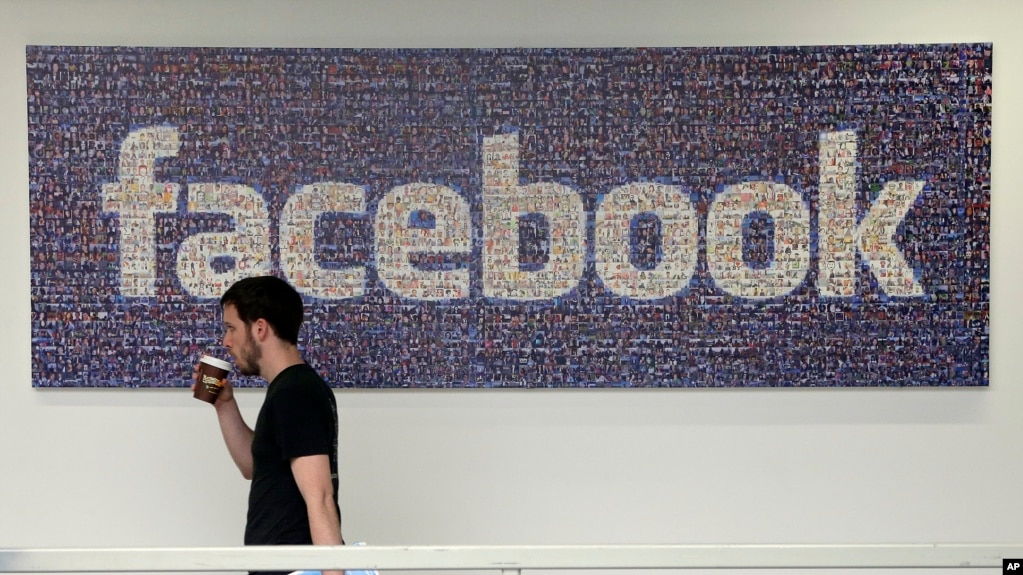 FILE - A Facebook employee walks past a sign at Facebook headquarters in Menlo Park, California, March 15, 2013.