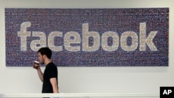 FILE - A Facebook employee walks past a sign at Facebook headquarters in Menlo Park, California. 