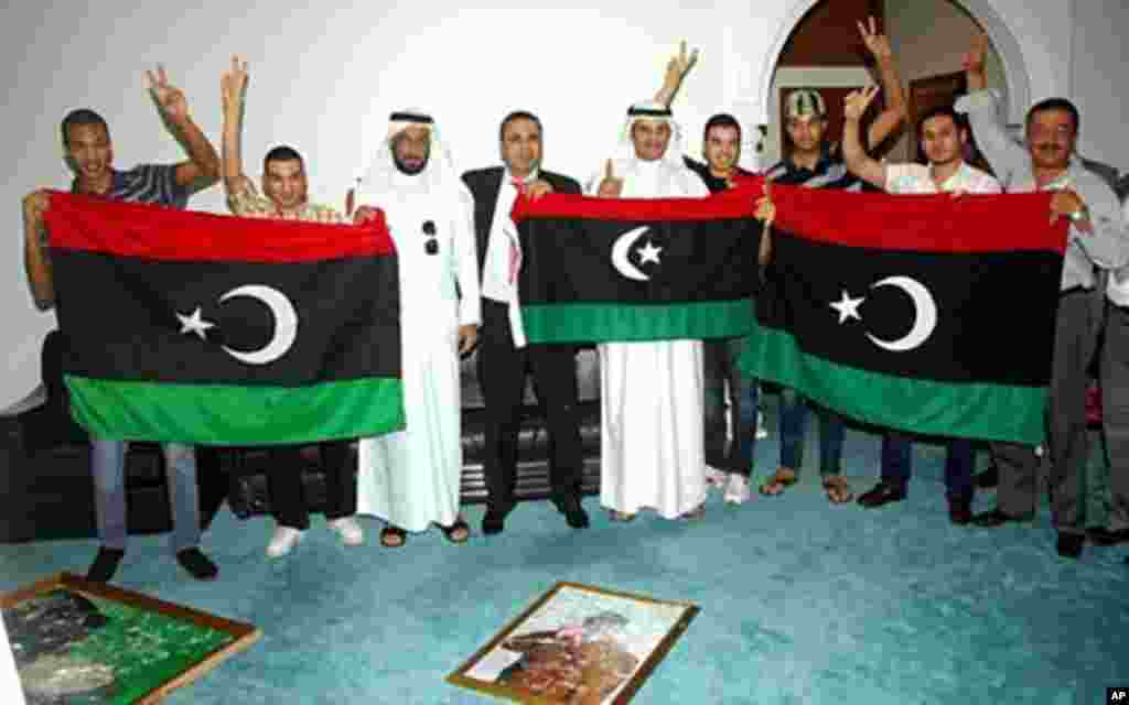 The old Libyan flag adopted by the rebel forces fighting against soldiers loyal to leader Moammar Gadhafi is held up as Gadhafi's images lay smashed on the floor at the Libyan embassy, Kuwait City, August 22, 2011. (AFP)