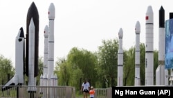 FILE - A woman walks with a child as they visit a park displaying replicas of foreign and domestic space vehicles in Beijing, China, June 26, 2016. China and the United States announced a new round of talks with China about civil space exploration.