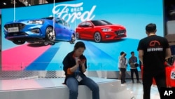 FILE - Visitors check out the Ford booth during the Auto China 2018 show, in Beijing, China, April 25, 2018. (AP Photo/Ng Han Guan)