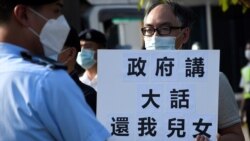 懷疑被送中港人鄭子豪父親在警員包圍下手持標語，質疑港府說謊要求中國當局釋放12港人。（美國之音湯惠芸拍攝）