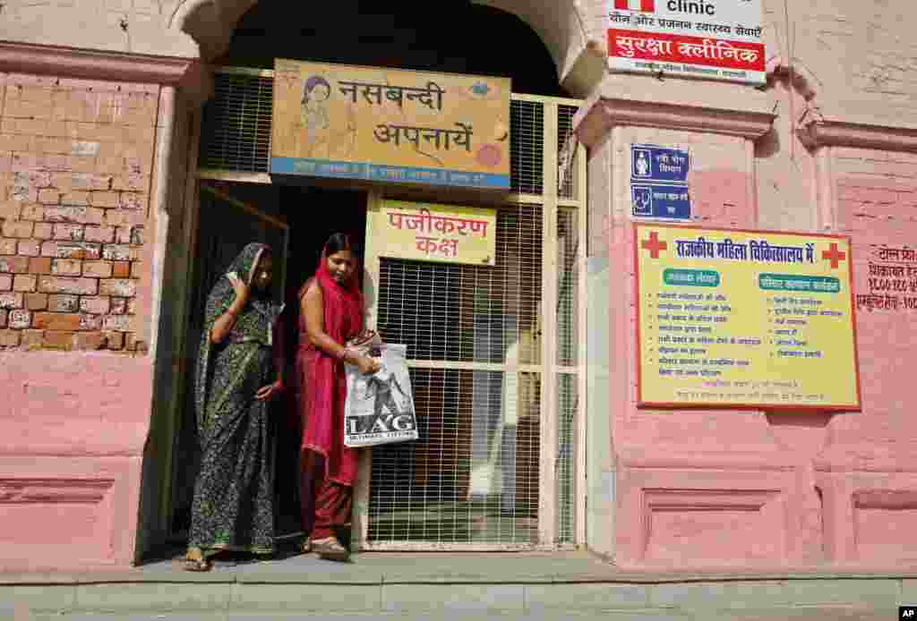 Indian women walk past a billboard advocating sterilization hung at the entrance of the District Women’s Hospital in Varanasi, India, Nov. 12, 2014.
