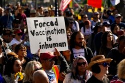 FILE - People listen to a speaker at a rally held to protest the city's new vaccine mandate, in Los Angeles, Nov. 8, 2021.