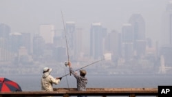Par ribolovaca u zalivu Elliot, dok ih okružuje dimom zasićen vazduh, sa Seattleom u daljini, 14. augusta 2018.