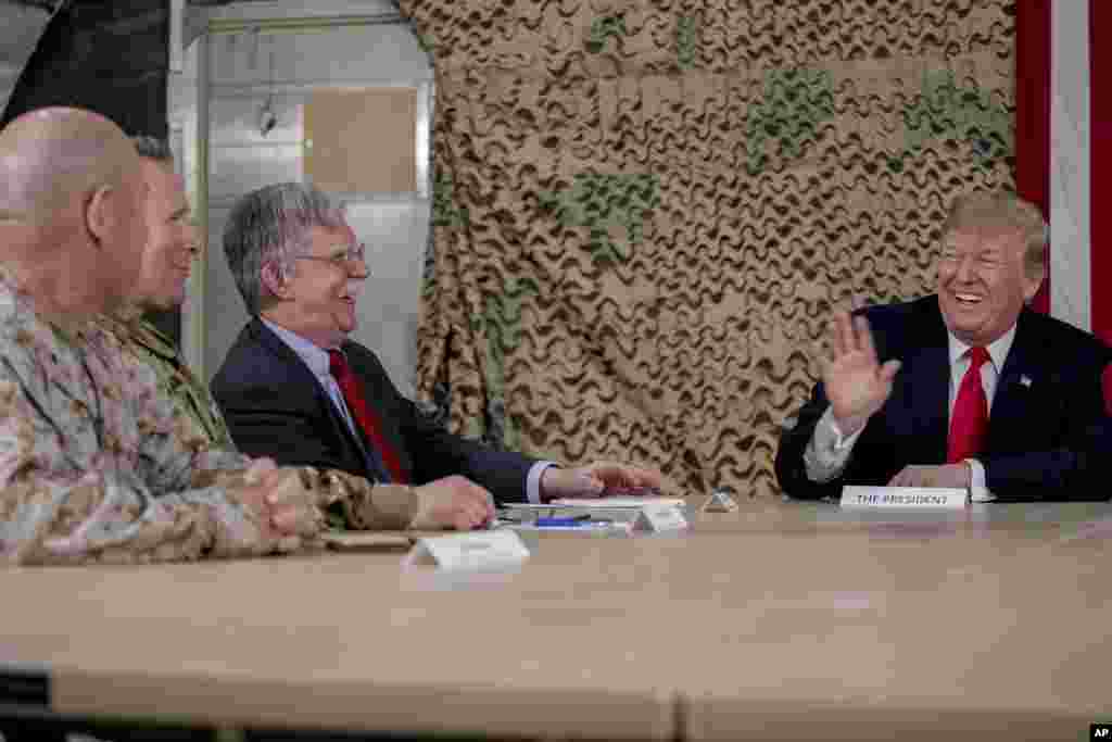 El residente Donald Trump, a la derecha, bromea con el asesor de seguridad nacional John Bolton, el tercero desde la izquierda y un líder militar de alto nivel, mientras habla con miembros de los medios de comunicación en la base aérea de Al Asad, Irak.