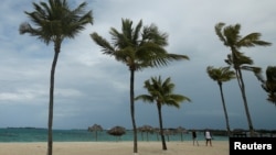 FILE - People walk along a beach in Nassau, Bahamas.