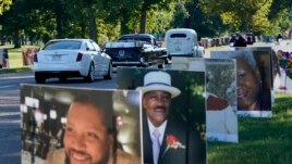 A procession of vehicles drive past photos of Detroit victims of COVID-19, Monday, Aug. 31, 2020 on Belle Isle in Detroit.