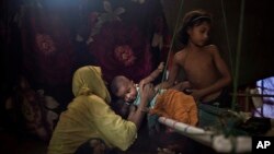 M’s daughter hands over her baby brother to their mother in their shelter in Kutupalong refugee camp, June 26, 2018. "M" was raped by six soldiers from Myanmar's security forces after they strangled her 2-year-old son to death.