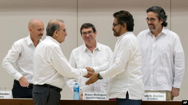 Humberto de la Calle, izquierda al frente, jefe del equipo de negociadores del gobierno colombiano da la mano a Iván Marquez, jefe negociador de las Fuerzas Armadas Revolucionarias de Colombia, FARC, tras la firma en Cuba de un pre-acuerdo -en diciembre 15 de 2015- sobre las reparaciones a 6 millones de víctimas del conflicto colombiano. 