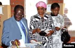 FILE - Zimbabwe's President Robert Mugabe casts his vote as his wife Grace and daughter Bona (L-R) look on in Highfields outside Harare, July 31, 2013.