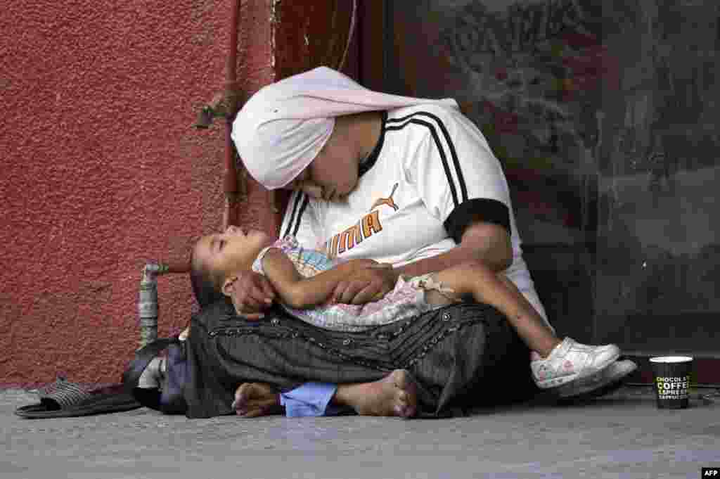 A Syrian refugee woman holds her child as they doze off on the sidewalk of a street in the southern Lebanese city of Sidon. The exodus of Syrian refugees accelerated dramatically in recent months, with over 1 million refugees arriving in the first five months of 2013 alone.