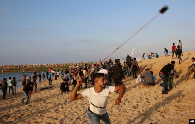 Protesters gather while others hurl stones at Israeli troops near the fence of the Gaza Strip border with Israel during a protest on the beach near Beit Lahiya, northern Gaza Strip, Nov. 19, 2018.