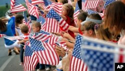 People wave flags as the Independence Day parade rolls down Main Street, July 4, 2014, in Eagar, Ariz. 