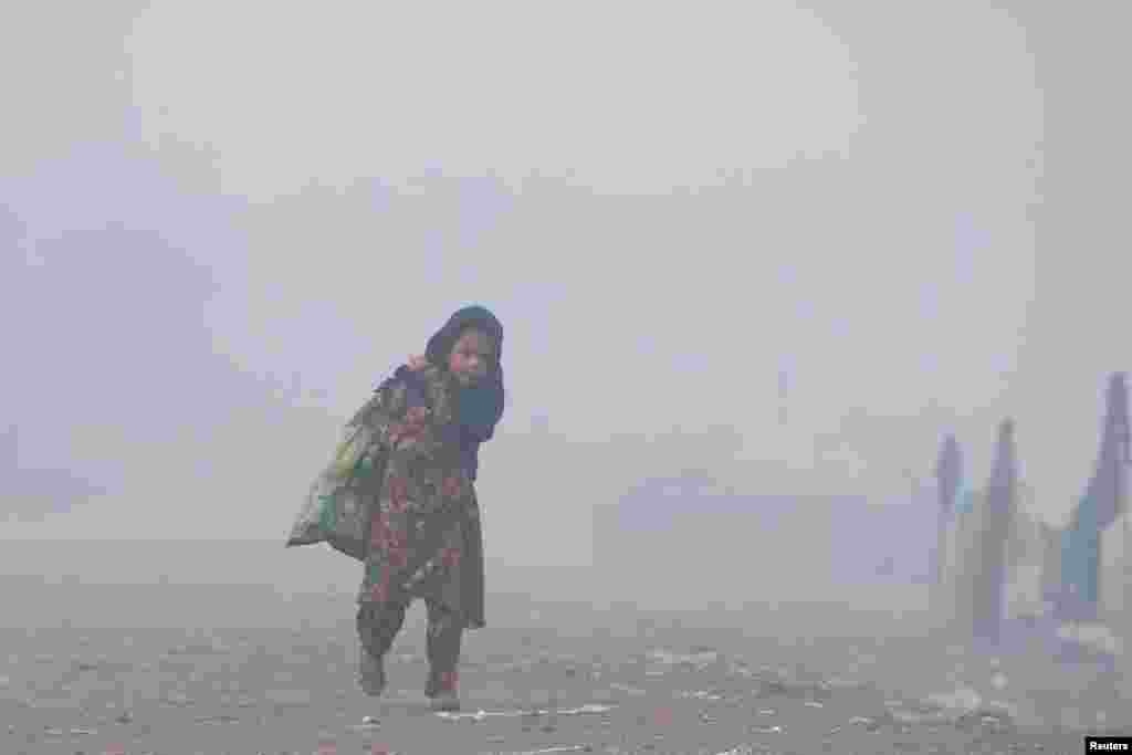 Seorang anak perempuan membawa karung daur ulang saat berjalan di tengah kabut pada pagi hari yang dingin di Peshawar, Pakistan. (Foto: Fayaz Aziz/Reuters)