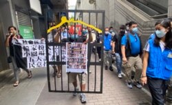 社民连成员曾健成手持道具”铁牢笼”，贴上被当局以国安法”煽动颠覆国家政权罪”控告的47名民主派初选人士海报，抗议当局囚禁民意代表 (美国之音/汤惠芸)