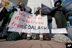FILE - Demonstrators chant and hold signs behind a display of coal ash and the heavy metals in it during a protest near Duke Energy's headquarters in Charlotte, N.C., Feb. 6, 2014 over Duke Energy's coal plants.