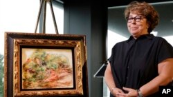 Sylvie Sulitzer, a delicatessen owner from the south of France, stands with a Renoir painting that was returned to her in a reparation ceremony at a news conference, Sept. 12, 2018, in New York. The 1919 oil painting "Femmes Dans Un Jardin" was seized in Paris by the Nazis from Sulitzer's grandfather.