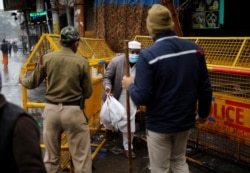 A man passes through barricades as policemen block a road after authorities in the capital ordered a weekend curfew, following the rise in the COVID-19 cases, in the old quarters of Delhi, India, Jan. 8, 2022.