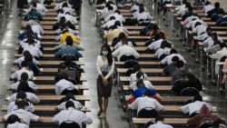 A teacher wears a protective mask as middle school students take an entrance examination for high school in Bangkok, Thailand, Thursday, March 5, 2020. Thailand reported its first death form COVID -19 illness on Sunday. (AP Photo/Sakchai Lalit)