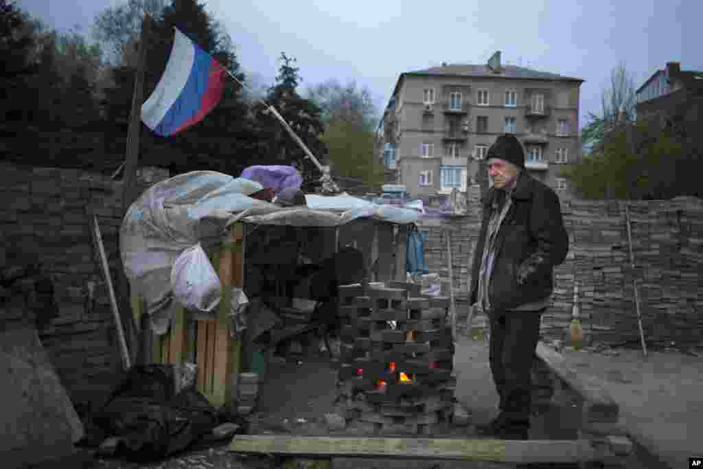 Seorang aktivis pro-Rusia menghangatkan diri dekat api unggun di barikade di Donetsk, Ukraina (20/4). (AP/Alexander Zemlianichenko)