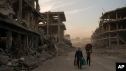 FILE - Two civilians carry belongings they collected from their damaged house in the Old City of Mosul, Iraq, Nov. 15, 2017. 