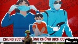 Một người dân đi ngang qua tranh cổ động phòng chống virus Corona ở Việt Nam.