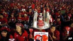 Anti-government ''red shirt'' protesters hold a picture of former Thai premier Thaksin Shinawatra as they wait for him to address them over a link during a rally near the Democracy monument, the site of bloody clashes with security forces last year, in Ba