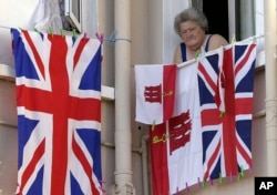 FILE - A woman resident of Gibraltar looks out of a window behind flags of England and Gibraltar, Aug. 4, 2004.