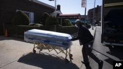 ARHIVA - Radnik u pogrebnom domu prebacuje kovčeg za vreme pandemije koronavirusa u Kvinsu, u Njujorku, (Foto: AP/Mark Lennihan)