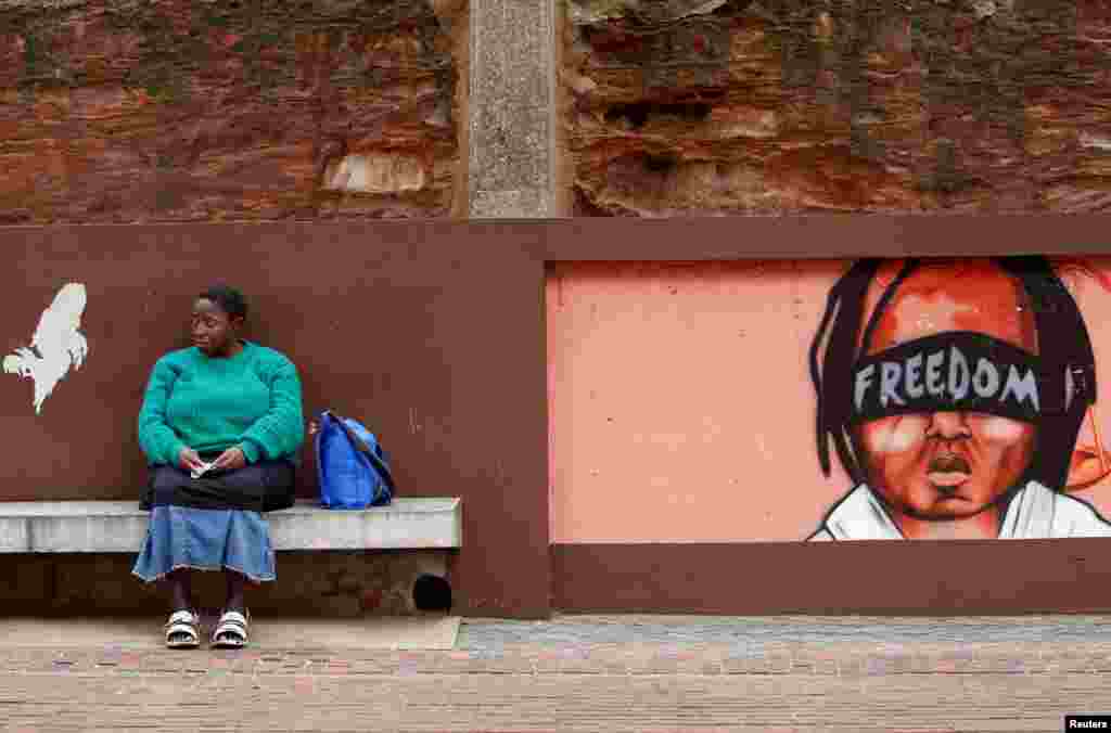 Seorang perempuan Afrika Selatan duduk di dekat lukisan mural di luar kantor pengadilan di Johannesburg.