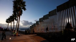 People walk along the U.S. border wall in an oceanside park in Tijuana, Mexico, at sunset, Nov. 30, 2018. 