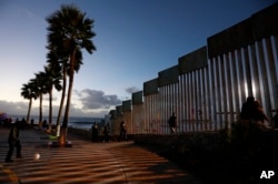 People walk along the U.S. border wall in an oceanside park in Tijuana, Mexico, at sunset, Nov. 30, 2018.