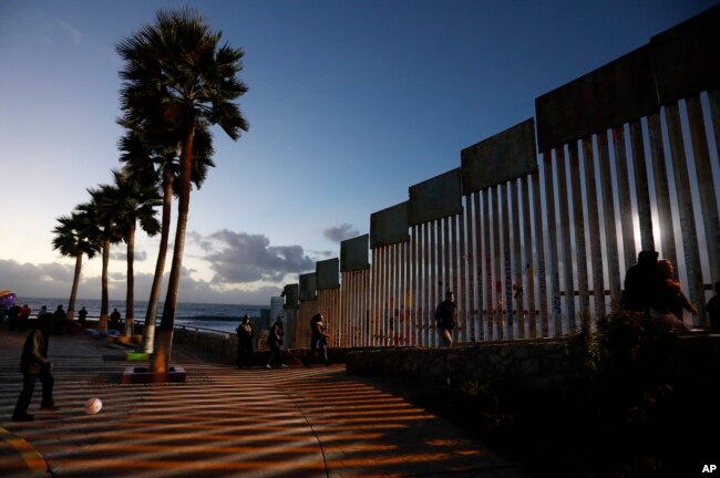 People walk along the U.S. border wall in an oceanside park in Tijuana, Mexico, at sunset, Nov. 30, 2018.