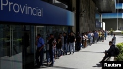People line up to withdraw cash from an automated teller machine outside a Banco Provincial branch in Caracas, Venezuela, Dec. 12, 2016.