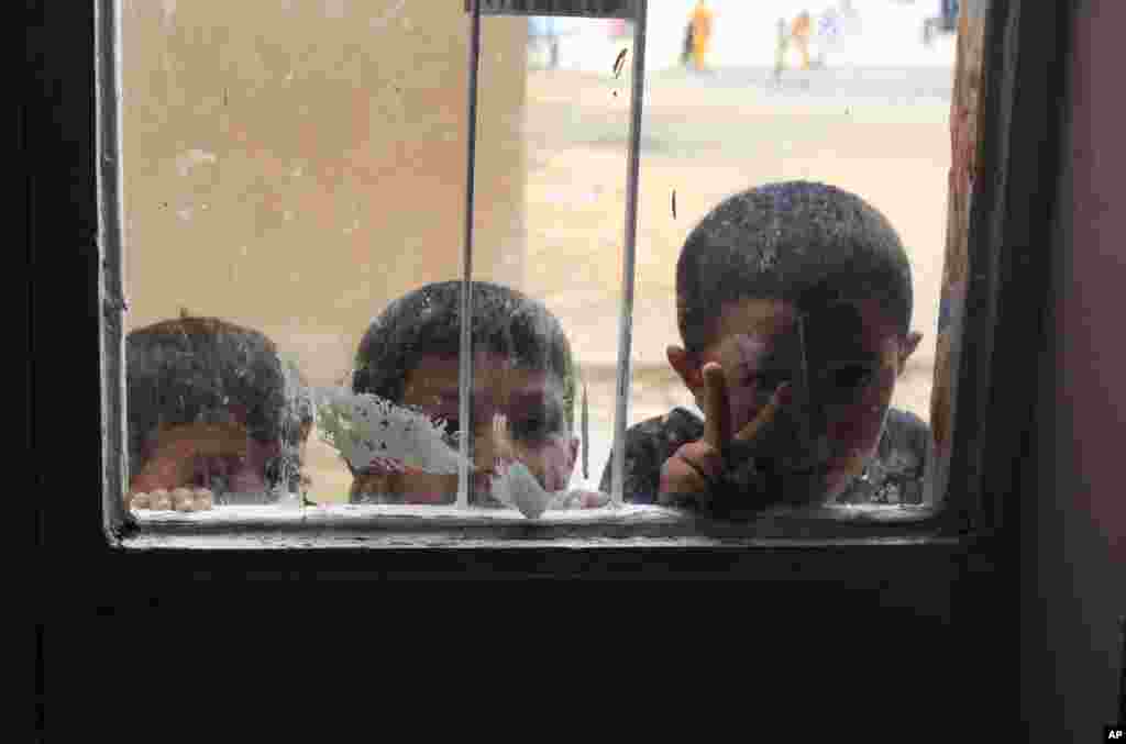 Syrian refugee children, one flashing the V-sign, peer through the window of a school building serving as a refugee center in the Turkish border town of Suruc, Turkey, Oct. 19, 2014.
