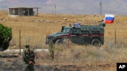 Syrian army soldier stands guard as Russian military police vehicle passes by near the town of Alhureyeh, Aug. 14, 2018. 