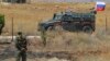 Syrian army soldier stands guard as Russian military police vehicle passes by near the town of Alhureyeh, Aug. 14, 2018. 