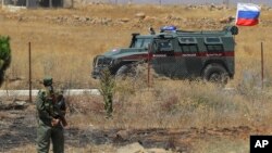 Syrian army soldier stands guard as Russian military police vehicle passes by near the town of Alhureyeh, Aug. 14, 2018. 