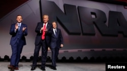 FILE - NRA Executive Director Chris Cox, left, and Executive Vice President and CEO Wayne LaPierre, right, welcome U.S. President Donald Trump onstage to deliver remarks at the National Rifle Association (NRA) Leadership Forum.