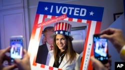 A woman wearing a U.S. patriotic top hat poses for a photograph in the foreground of a cardboard figure depicting Donald Trump Republican presidential candidate during the Election Night Party at the US Embassy in Budapest, Hungary, Nov. 8, 2016.