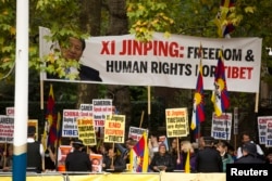 Human rights demonstrators hold up a protest banner bearing an image of Chinese President Xi Jinping before he passed by on a horse-drawn carriage with Britain's Queen Elizabeth II on the Mall en route to Buckingham Palace in London, Oct. 20, 2015.