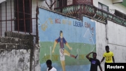 FILE - Men walk by a mural that reads "Get the hell of Liberia, Ebola! And don't come back" in Monrovia, Liberia, April 1, 2016. 