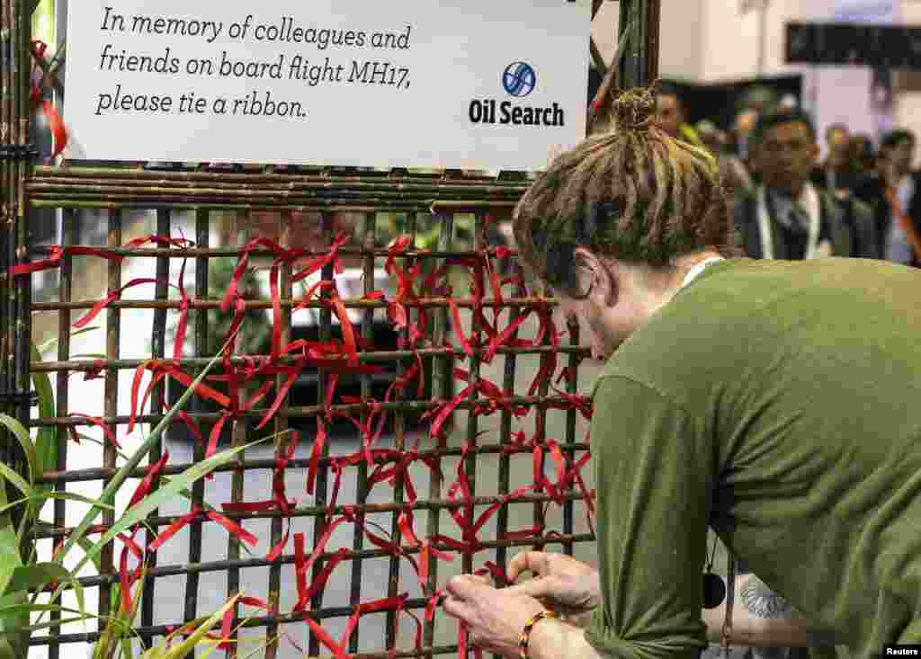 A delegate of the 20th International AIDS Conference ties a red ribbon to a memorial board as a tribute to colleagues killed in the Malaysia Airlines flight MH17, in Melbourne, Australia, July 20, 2014.