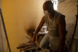 Juarez Viana breaks a stick to fit on the wood stove he has been using to cook for his family since last month, in São Paulo, Nov. 14, 2021. (Yan Boechat/VOA)