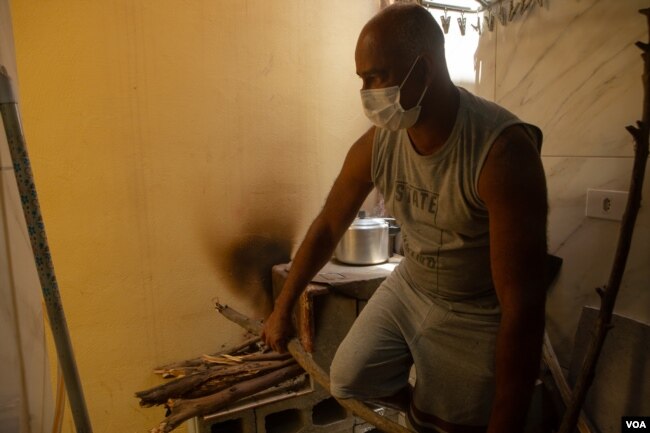 Juarez Viana breaks a stick to fit on the wood stove he has been using to cook for his family since last month, in São Paulo, Nov. 14, 2021. (Yan Boechat/VOA)
